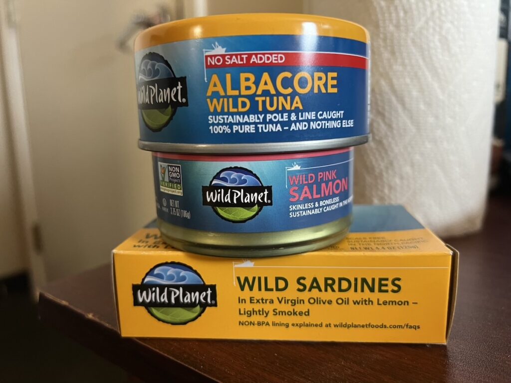 Stack of canned tuna, salmon, and sardines for protein-rich travel snacks.