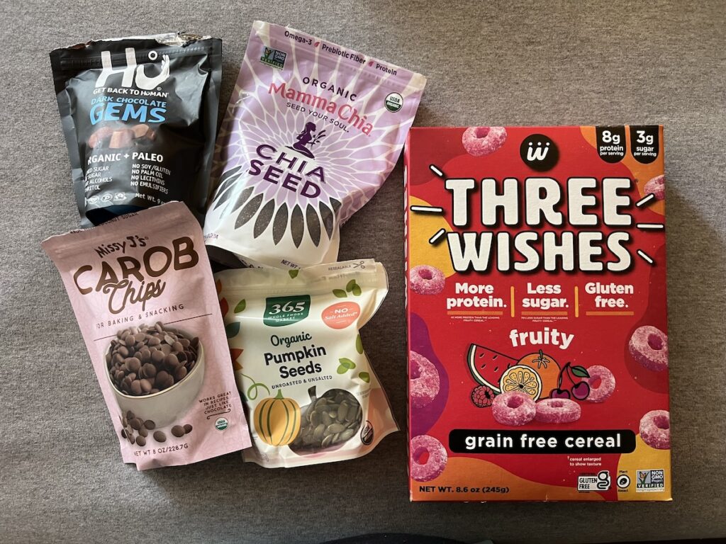 Ingredients for homemade allergy-friendly trail mix, including Three Wishes cereal, Hu chocolate gems, carob chips, chia seeds, and pumpkin seeds.