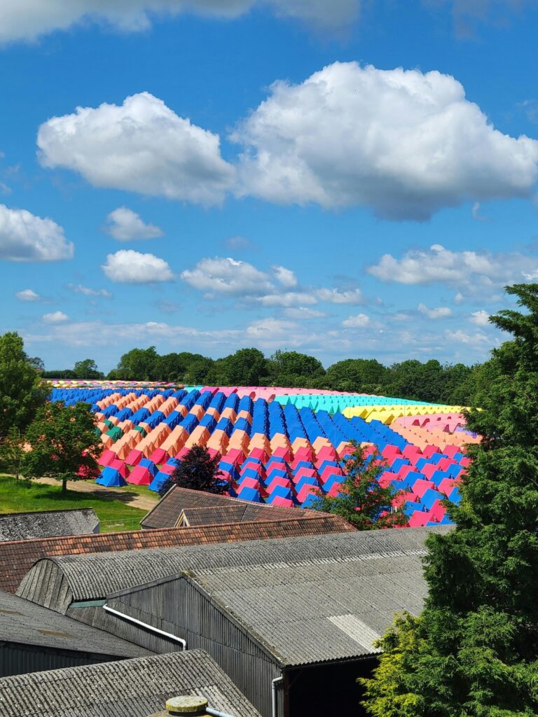 A vibrant sea of colorful tents set up in a green field under a blue sky at Glastonbury Festival in England.