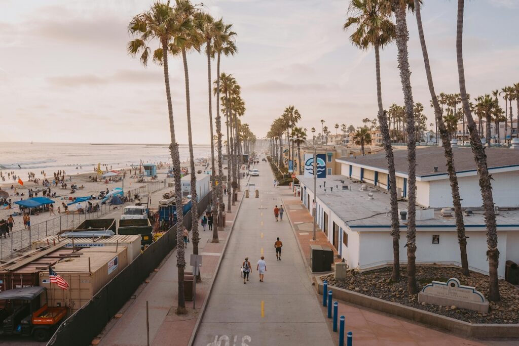 Elevated view of a palm tree-lined street in San Diego, California with people walking on it, with buildings on one side and the beach on the other