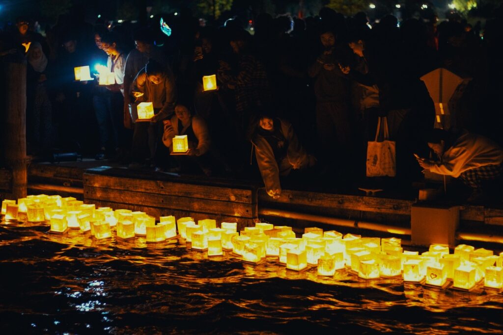People floating lanterns on water during Obon in Japan, a festival honoring ancestral spirits