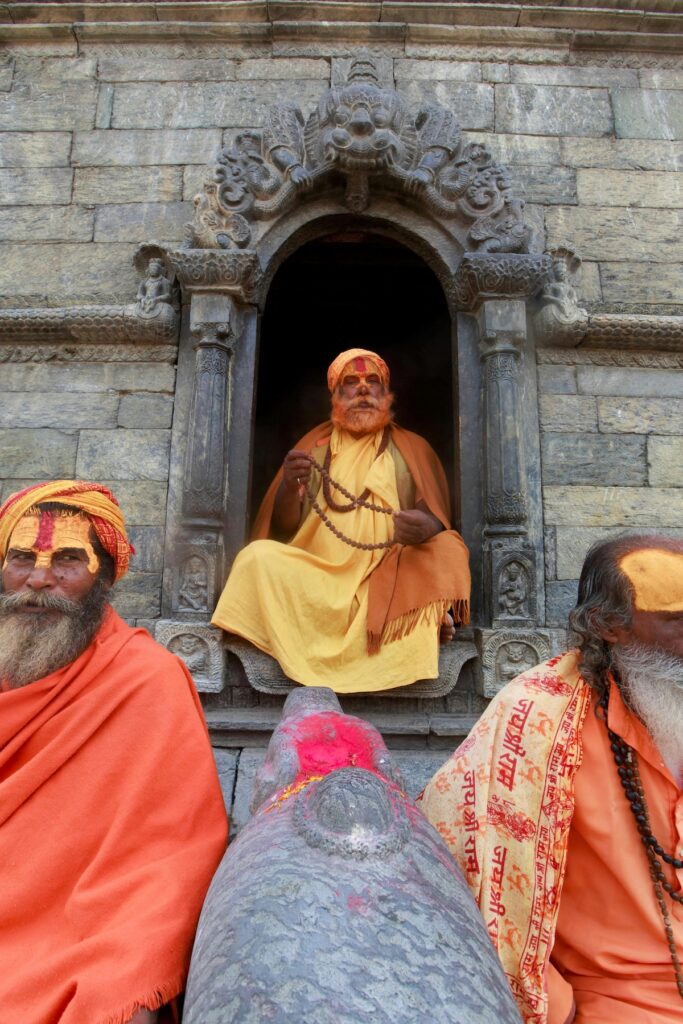 Large group of Hindu pilgrims sitting on the ground during Kumbh Mela, wearing traditional saffron robes and face paint for Maha Shivaratri